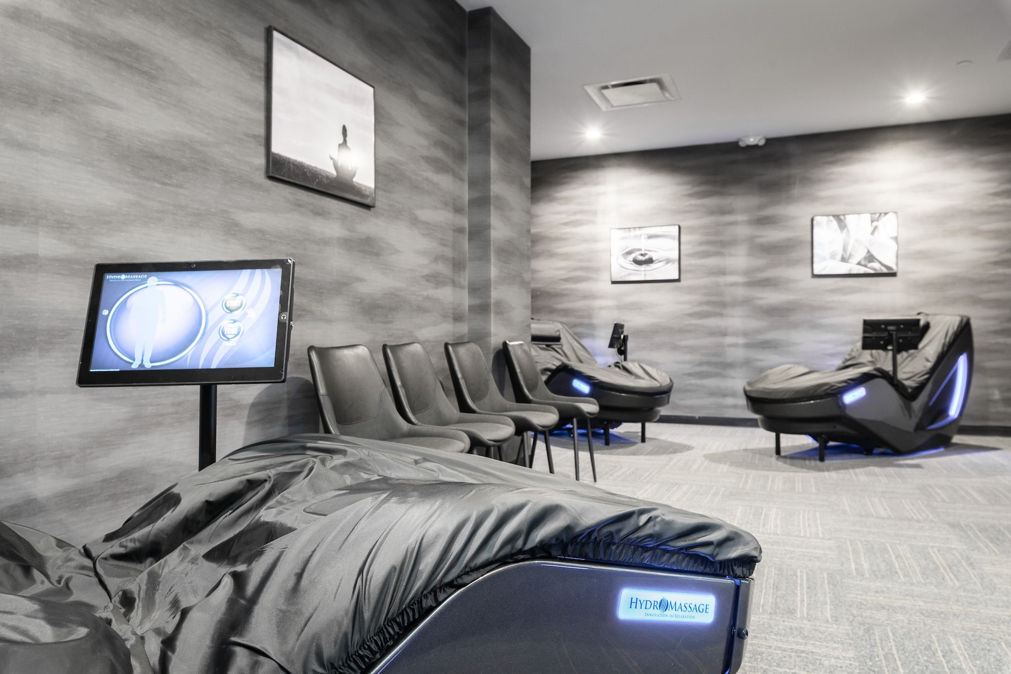 Hydromassage-and-recovery-lounge-at-Level-Fitness-Club-premier-full-service-gym-in-Yorktown Modern spa lounge with massage chairs and framed wall art, featuring gray decor and a relaxing ambiance.