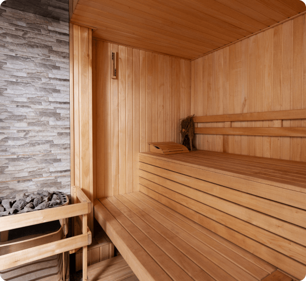 Modern wooden sauna with benches, a heater with stones, and a brick accent wall.